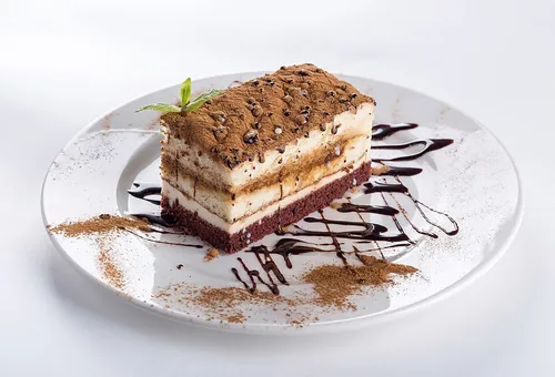 Piece of chocolate cake, sprinkled with cocoa powder, on a white plate decorated with chocolate sauce.